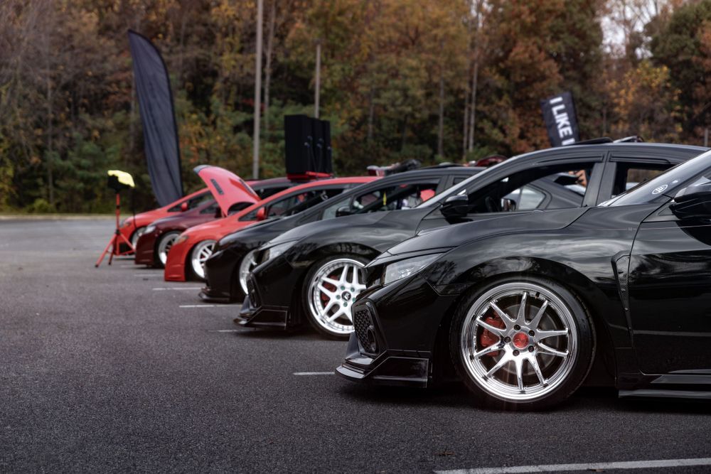 Row of modified sports cars lined up at a car meet showing custom wheels.