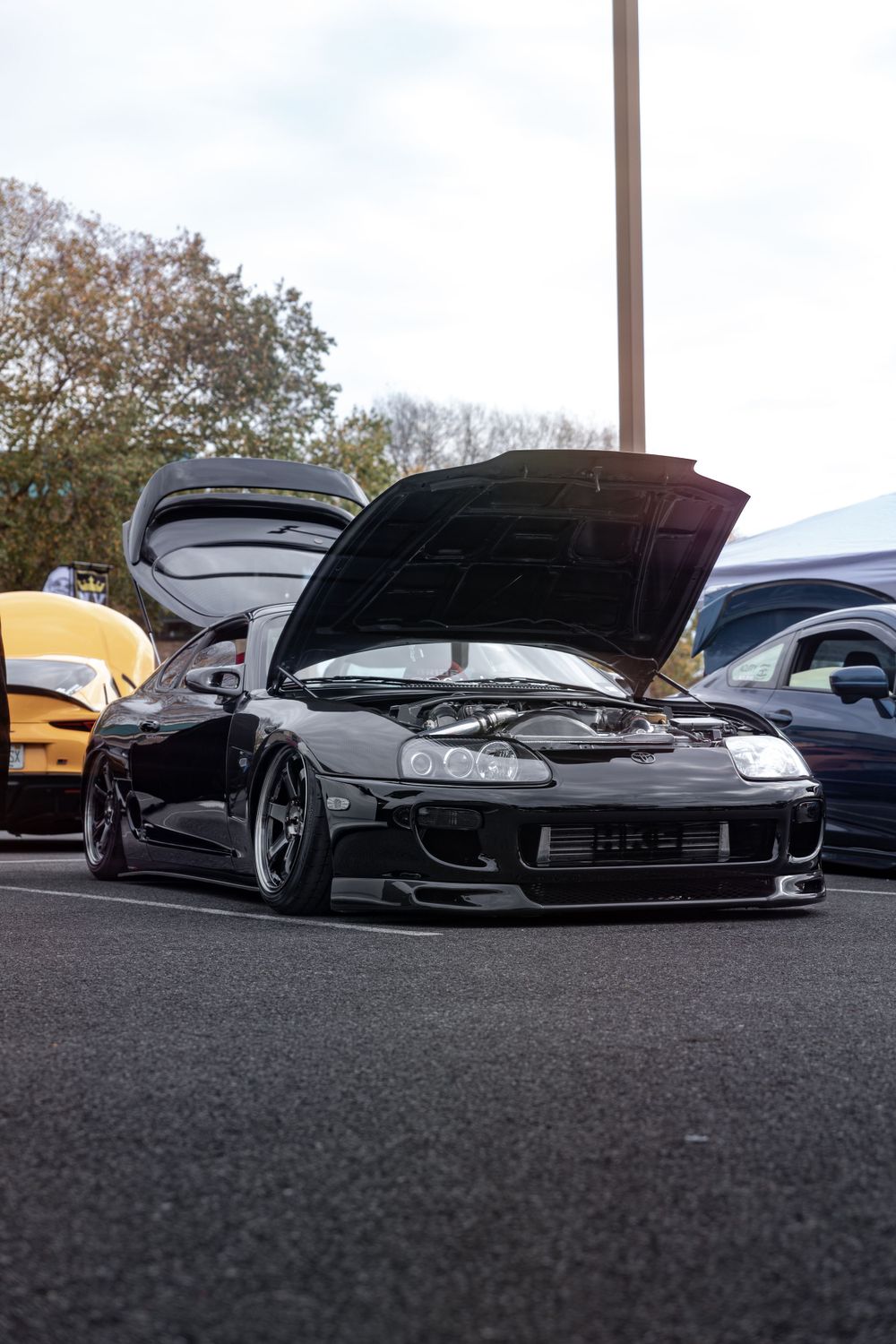 Modified black Toyota Supra with hood open at car show.