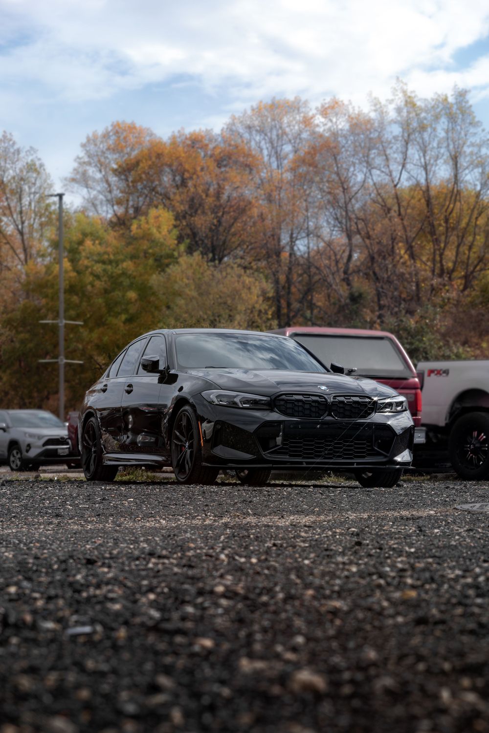 Black BMW M3 parked in a lot during autumn with trees in background.