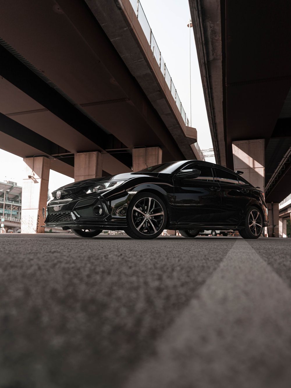 Side profile of a black Honda Civic photographed from ground level under concrete pillars.