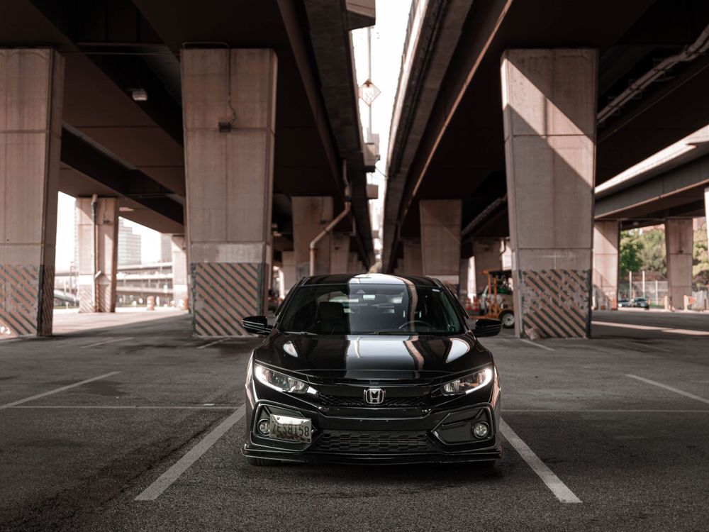 Front view of a modified black Honda Civic under a concrete overpass.