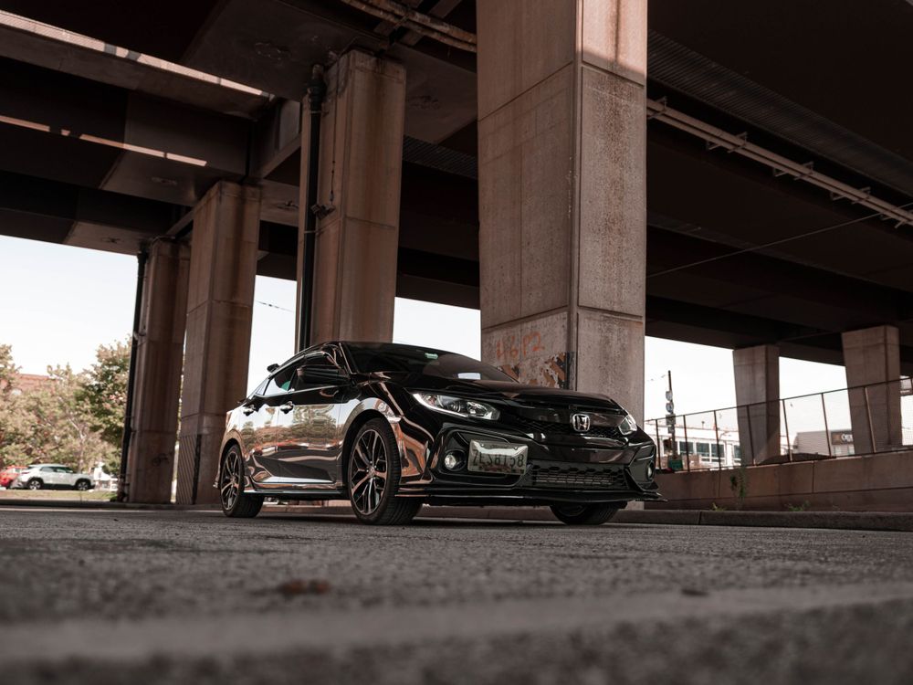 Low angle shot of a black Honda Civic with custom wheels under a highway overpass.