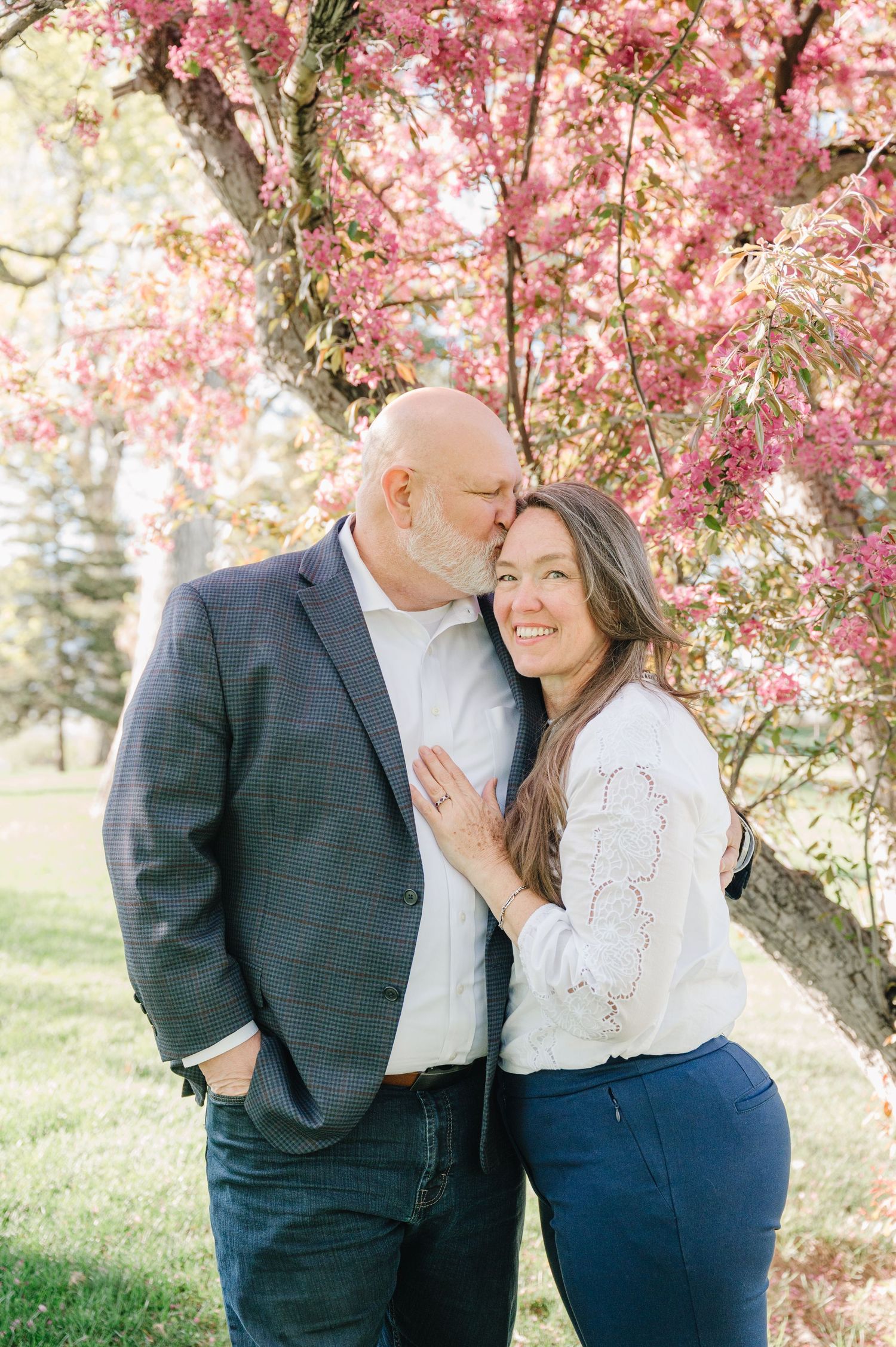 A couple shares a tender moment under blooming pink cherry blossoms during a springtime photo session.
