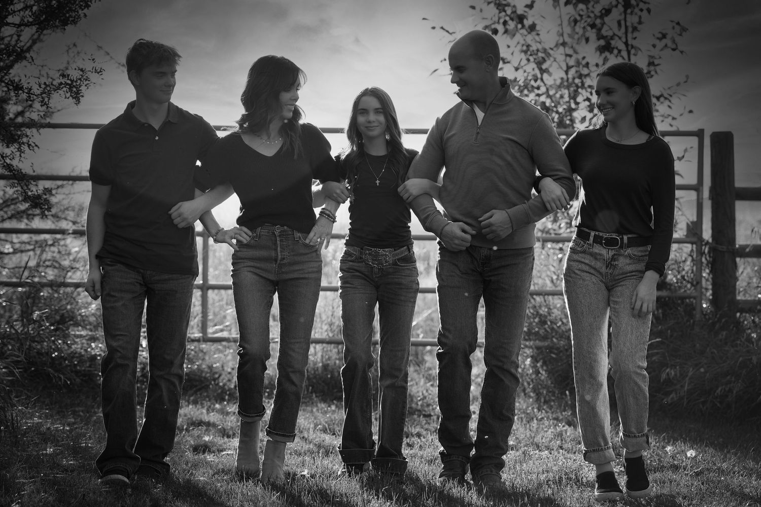 Five friends walk arm in arm down a country path in a nostalgic black and white photo.