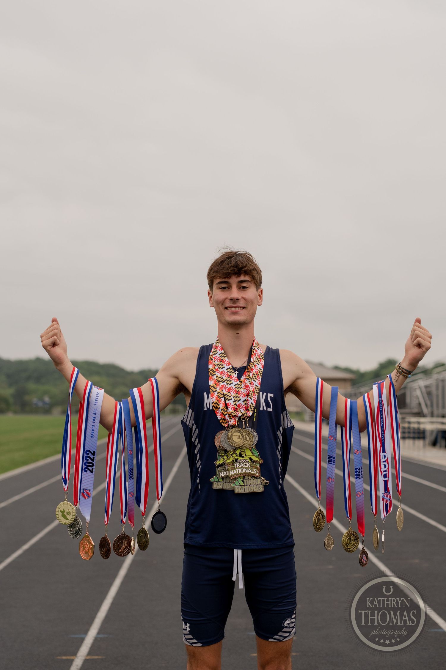 Athlete displays numerous medals and ribbons while standing triumphantly on an outdoor track.