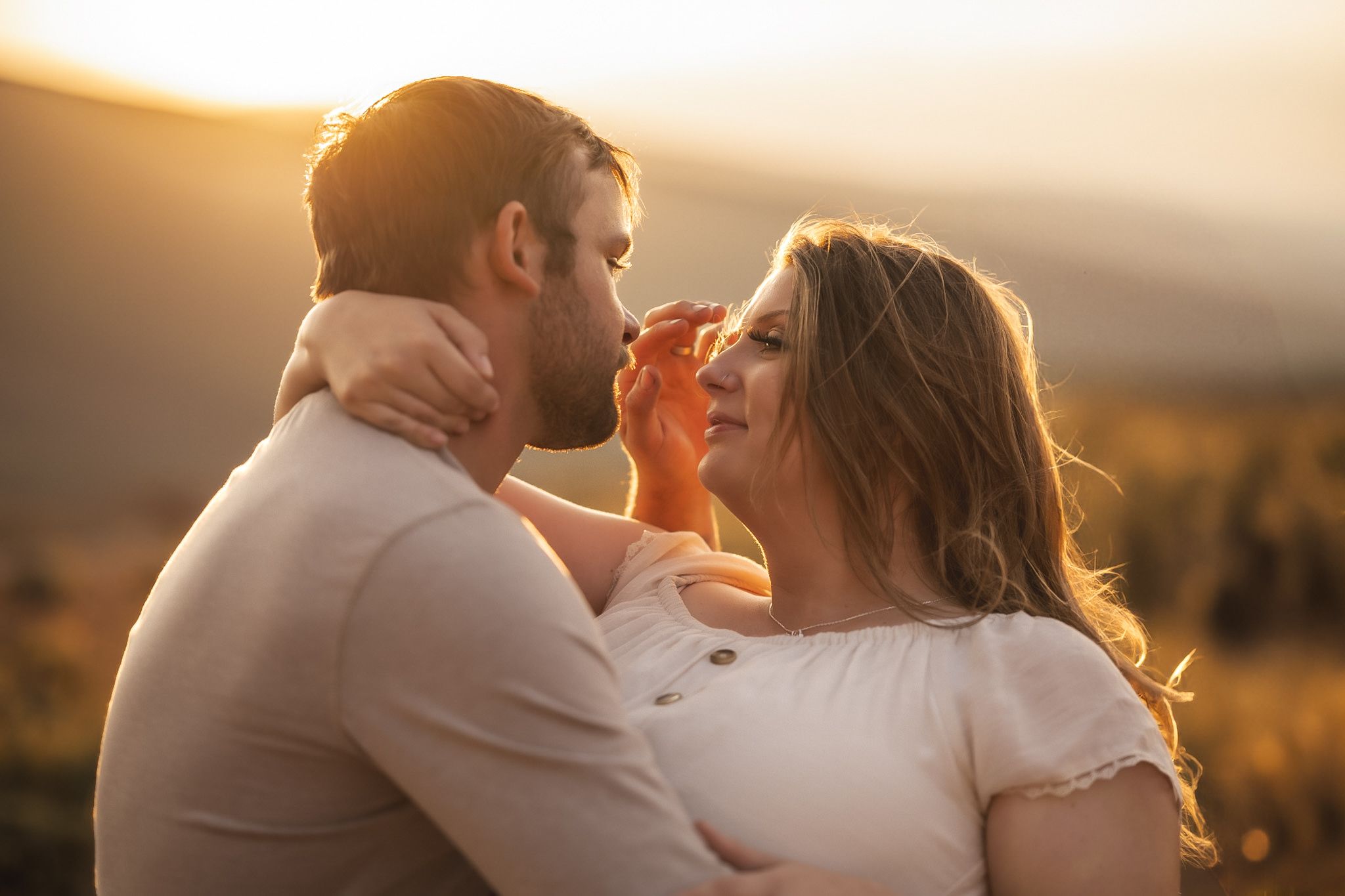 Couple embracing during golden hour with mountains in background.
