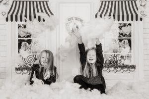 Black and white portrait of two children lying on snow with striped awnings overhead.