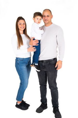 Family of three posing together against white background in coordinated white and blue outfits.