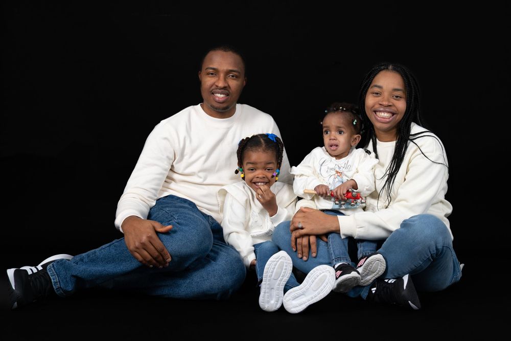 Studio portrait of a family wearing white tops and jeans against a black background.