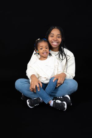 Portrait of two people in matching white sweaters and jeans against black background.