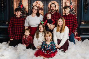 Holiday family portrait with matching buffalo plaid shirts against decorated Christmas backdrop.