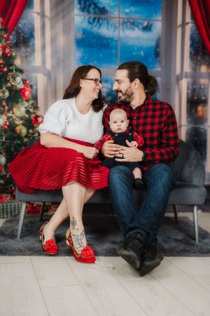 Holiday portrait with festive red and plaid attire against Christmas tree backdrop.