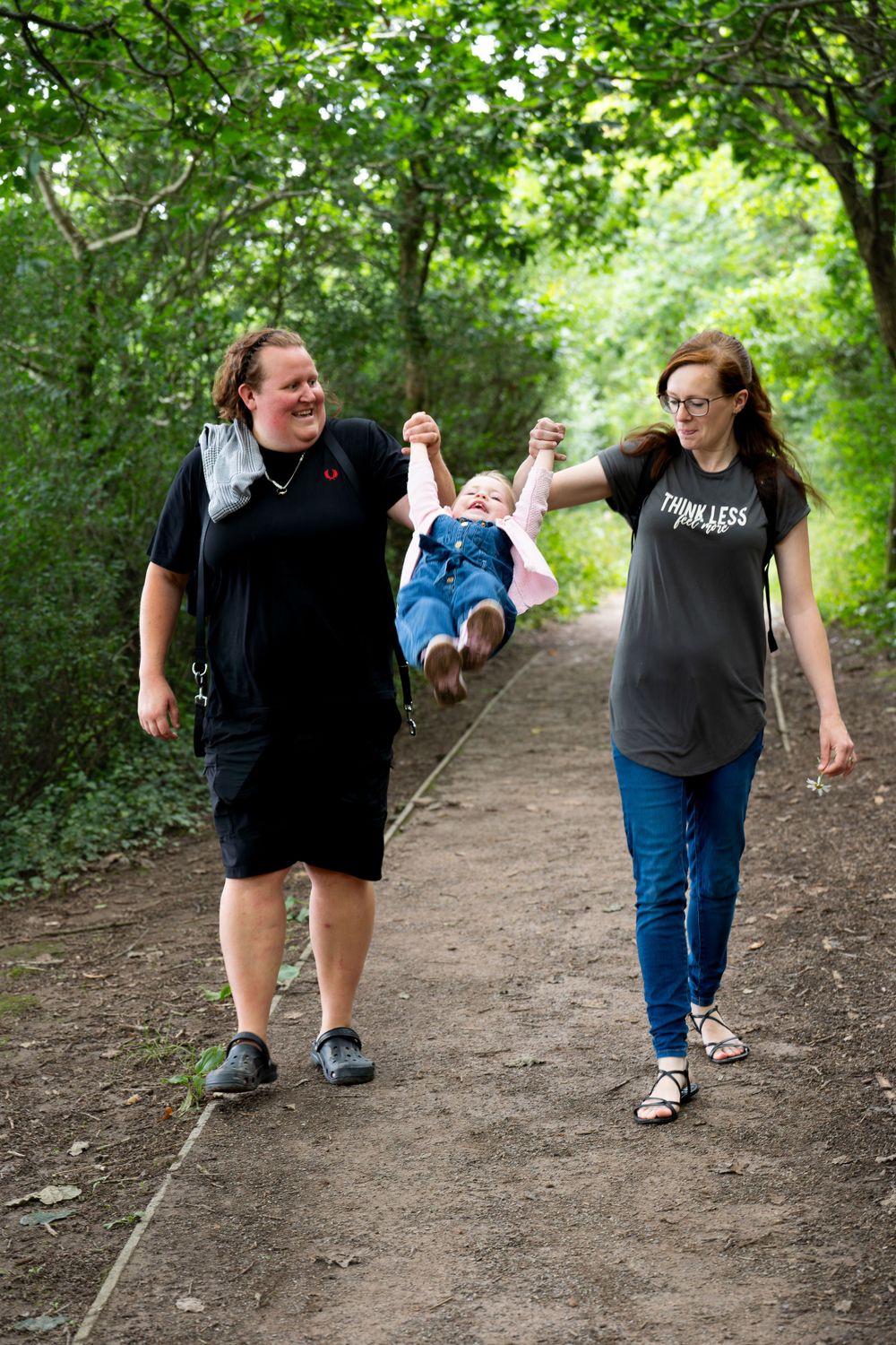 Family enjoying a nature walk together on a wooded trail while swinging a small child between them.