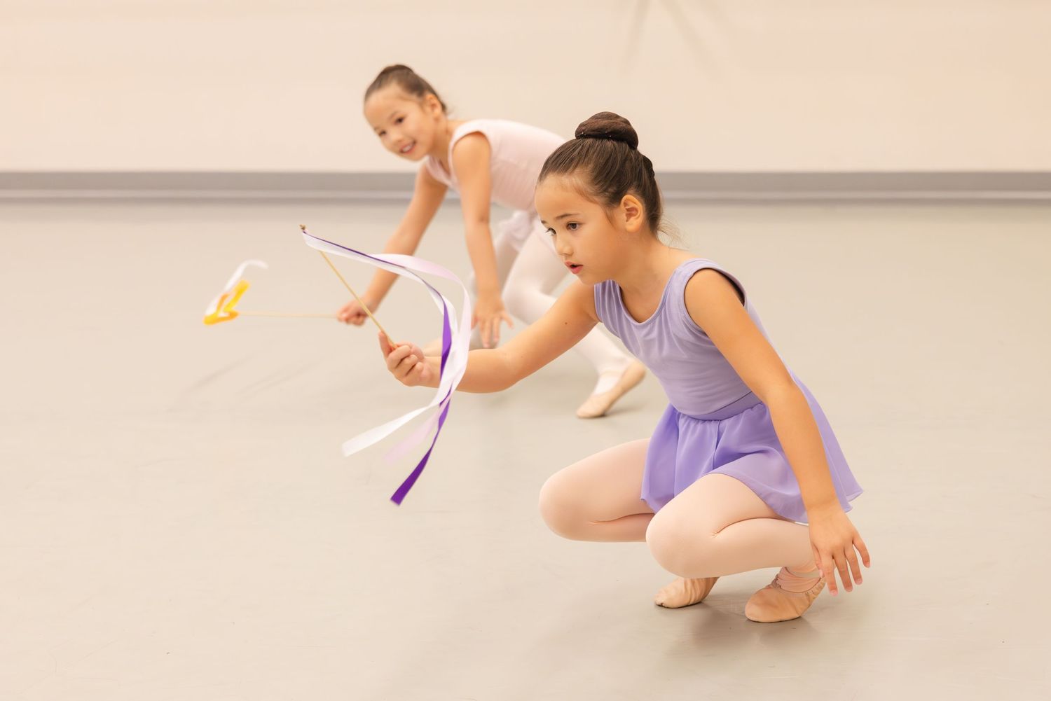 Two ballet dancers in pastel leotards practice with colorful ribbons in a dance studio.