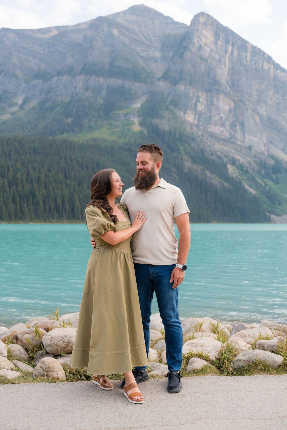 Couple embracing by turquoise Lake Louise with rocky mountains and evergreen forests in Banff, Alberta, Canada.