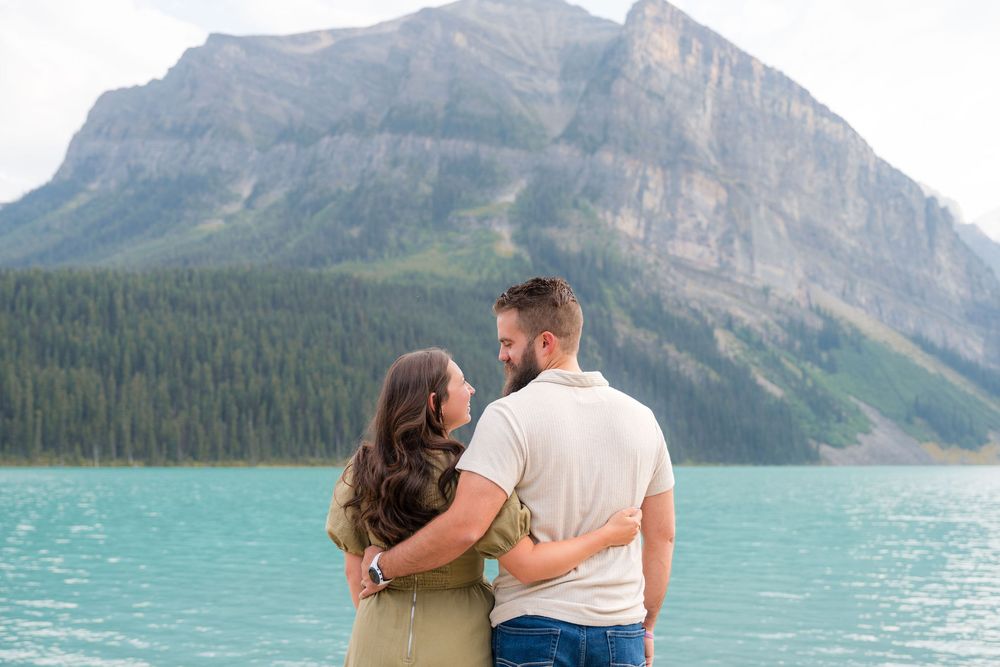 Couple embracing by turquoise Lake Louise with stunning mountain backdrop in Banff National Park, Alberta, Canada.