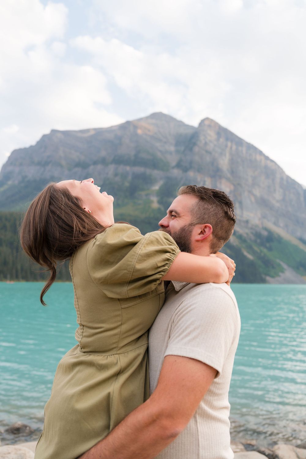 Happy couple embracing and laughing together at scenic Lake Louise with turquoise water and mountain views.