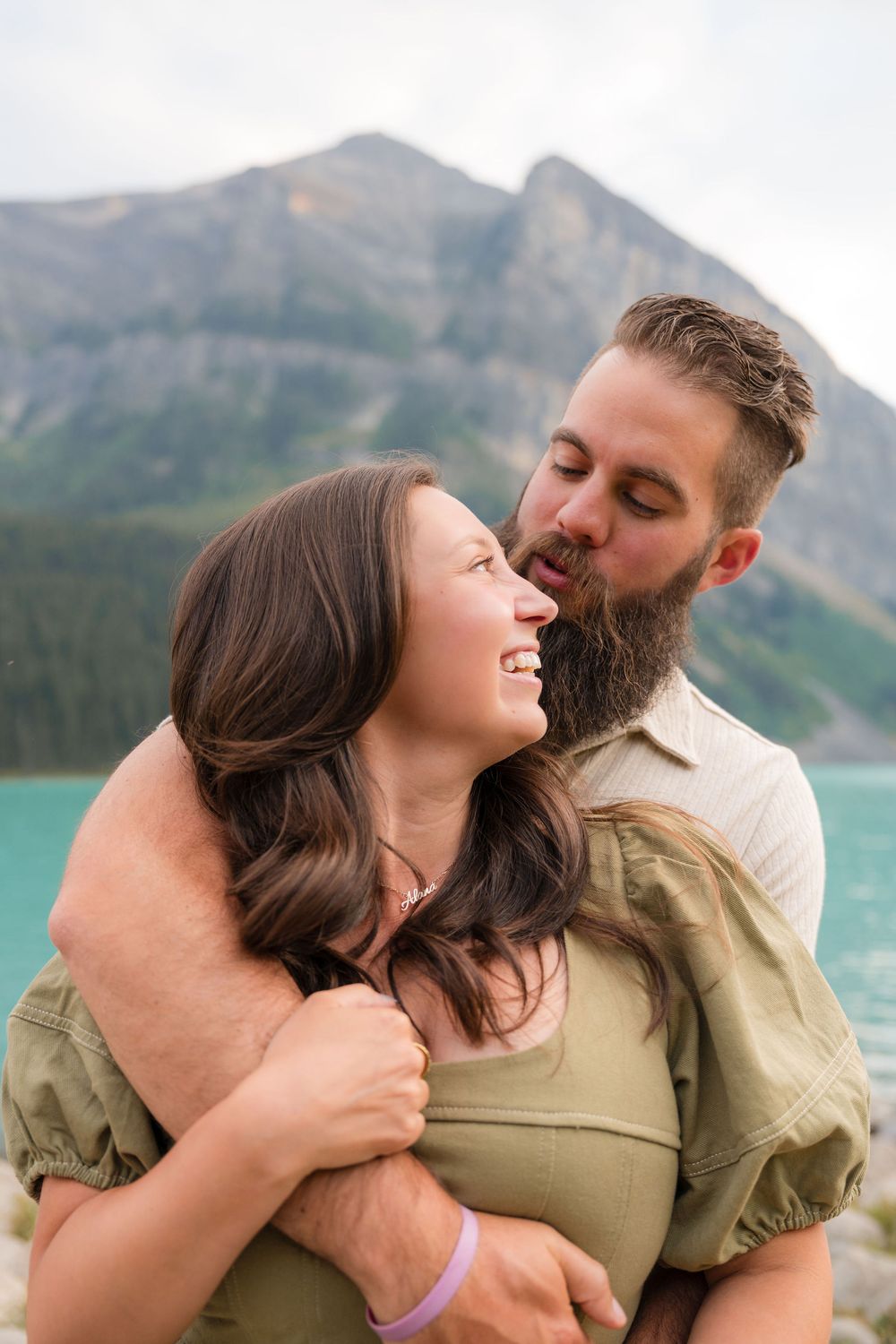 Couple embracing and laughing by turquoise Lake Louise with mountain backdrop.
