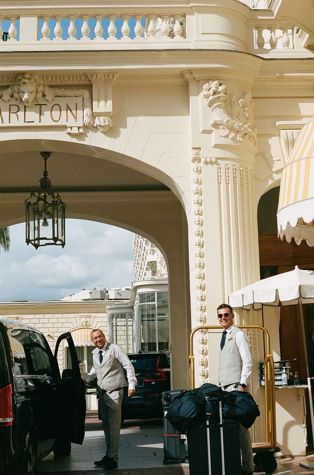 White columns and archways at the entrance of Carlton Hotel with luggage and vehicles parked outside.