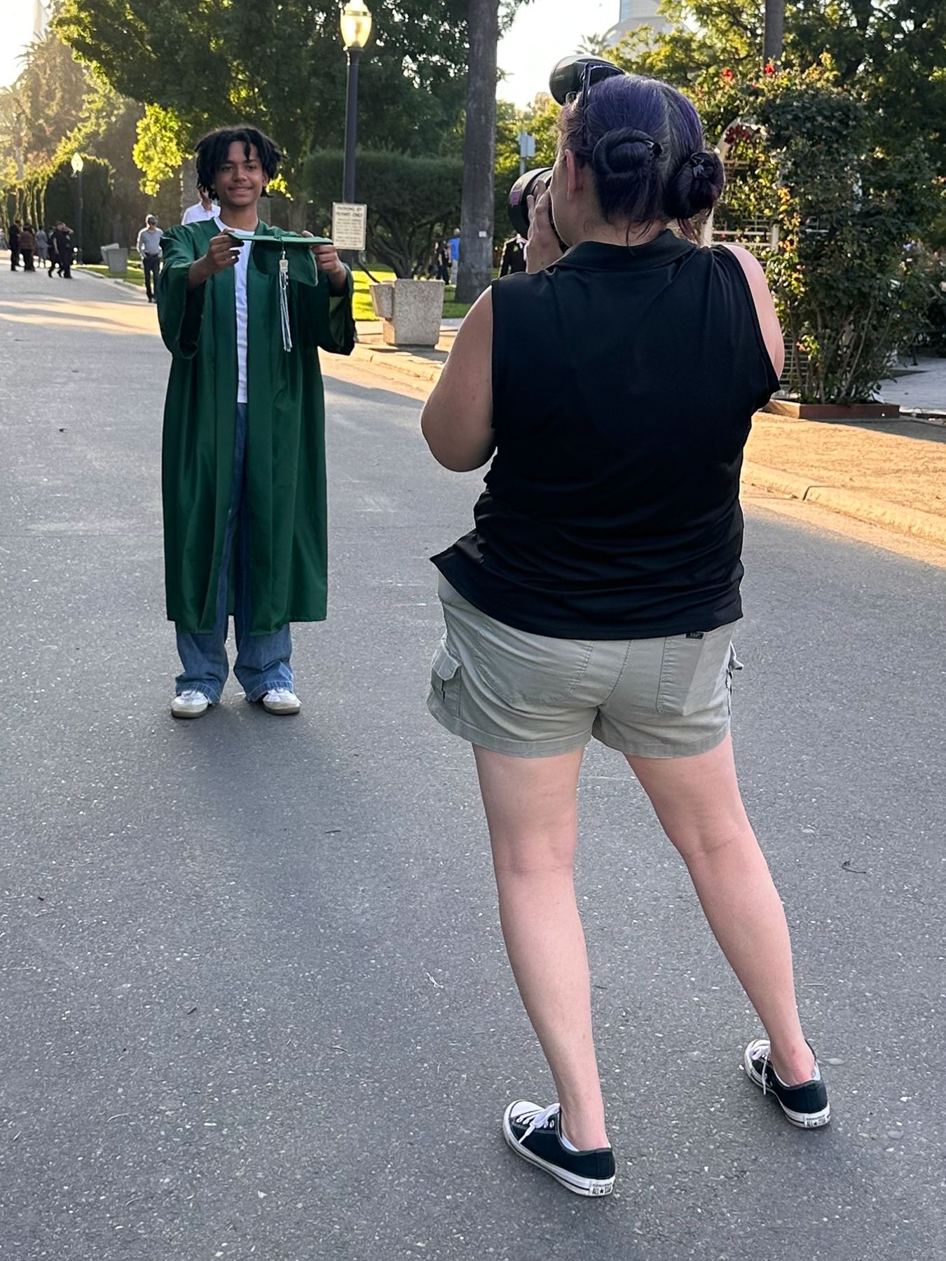 Graduate in green cap and gown poses for photo with family member outdoors at graduation ceremony.