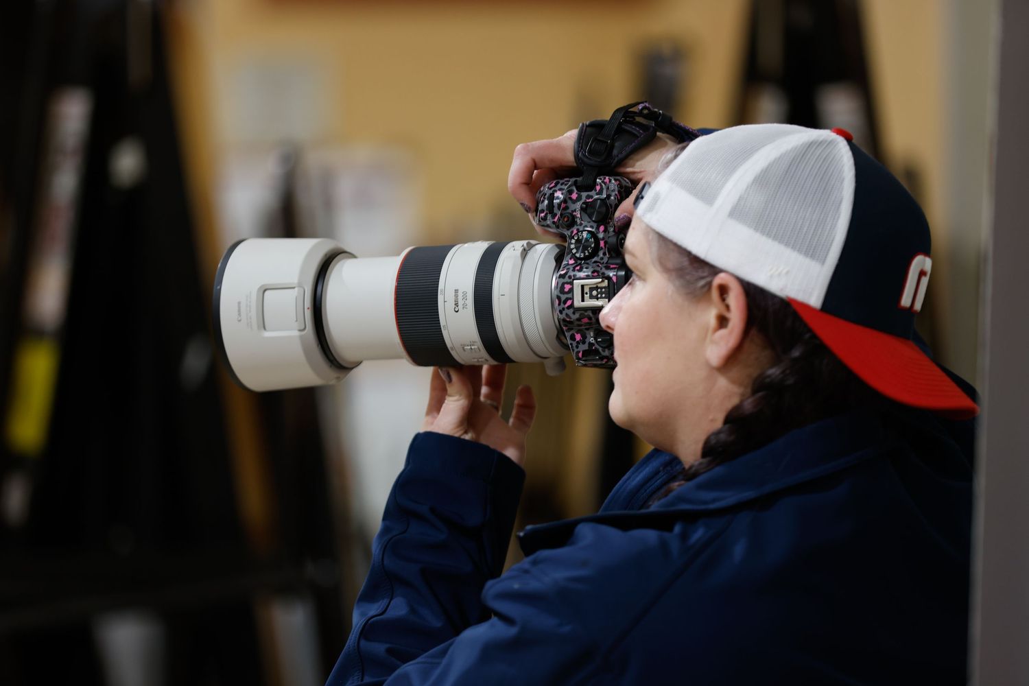 A photographer wearing a white and red baseball cap uses a telephoto lens on a digital camera to capture images.