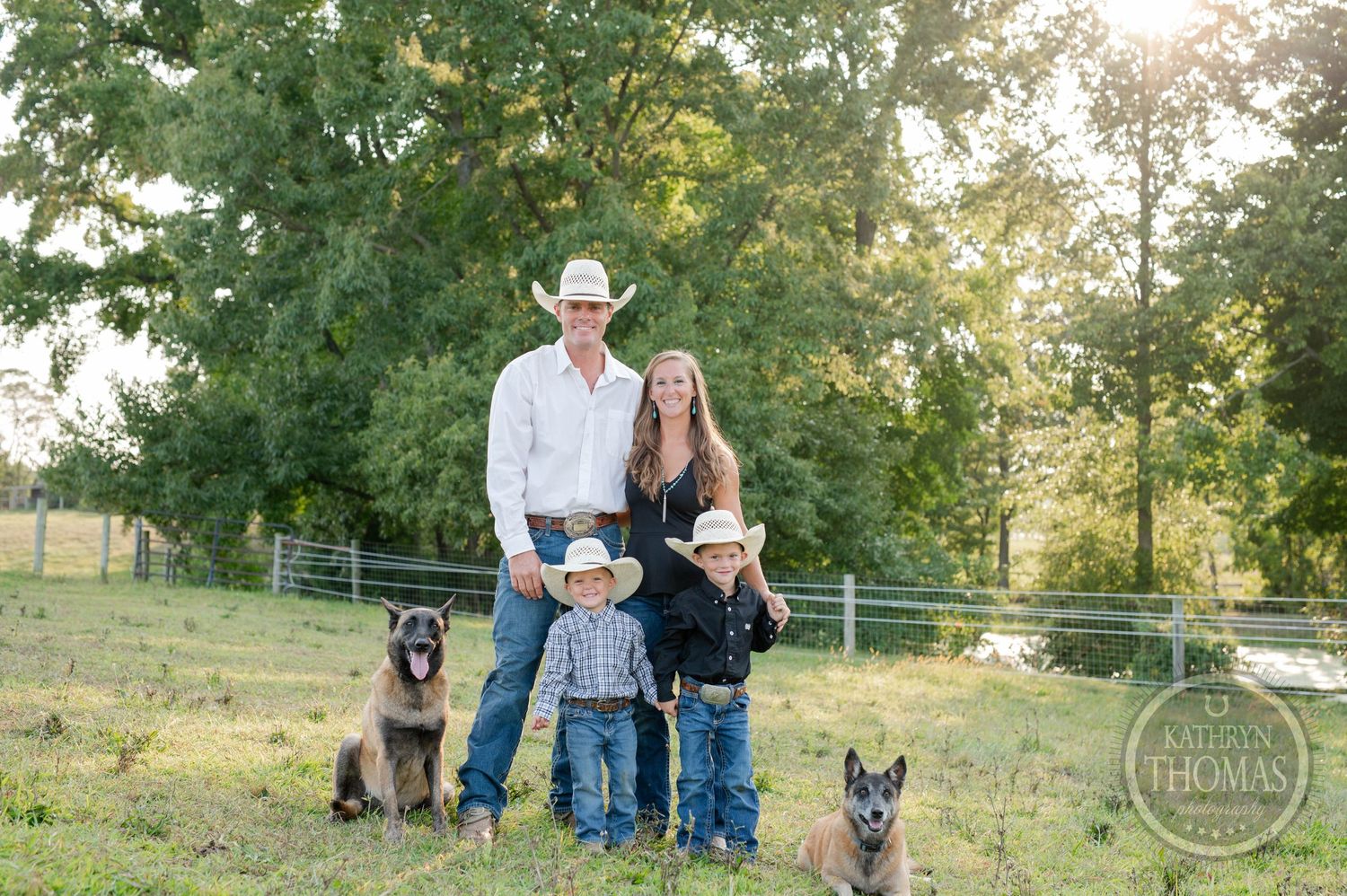 Country family standing with their German Shepherd dogs in fenced pasture at sunset.