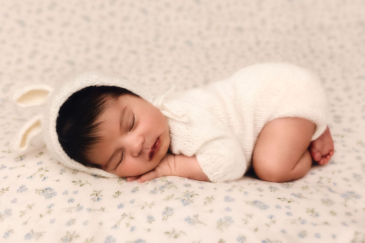 Newborn baby girl sleeping in mohair bunny suit on white floral blanket with blue accent in Charlottesville, Virginia.