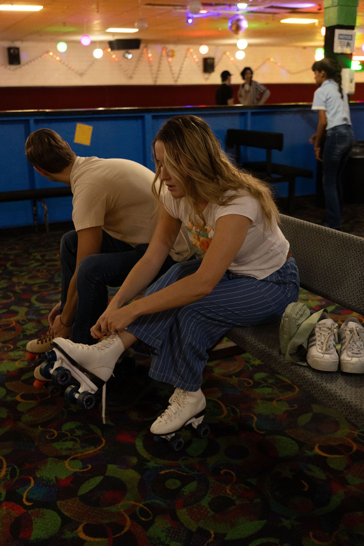 People putting on roller skates at a retro skating rink with colorful carpeting and neon lighting.