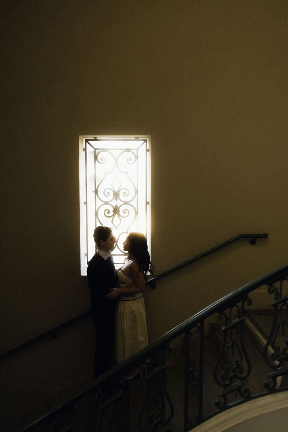 Two silhouettes stand in front of an illuminated decorative window on a staircase.