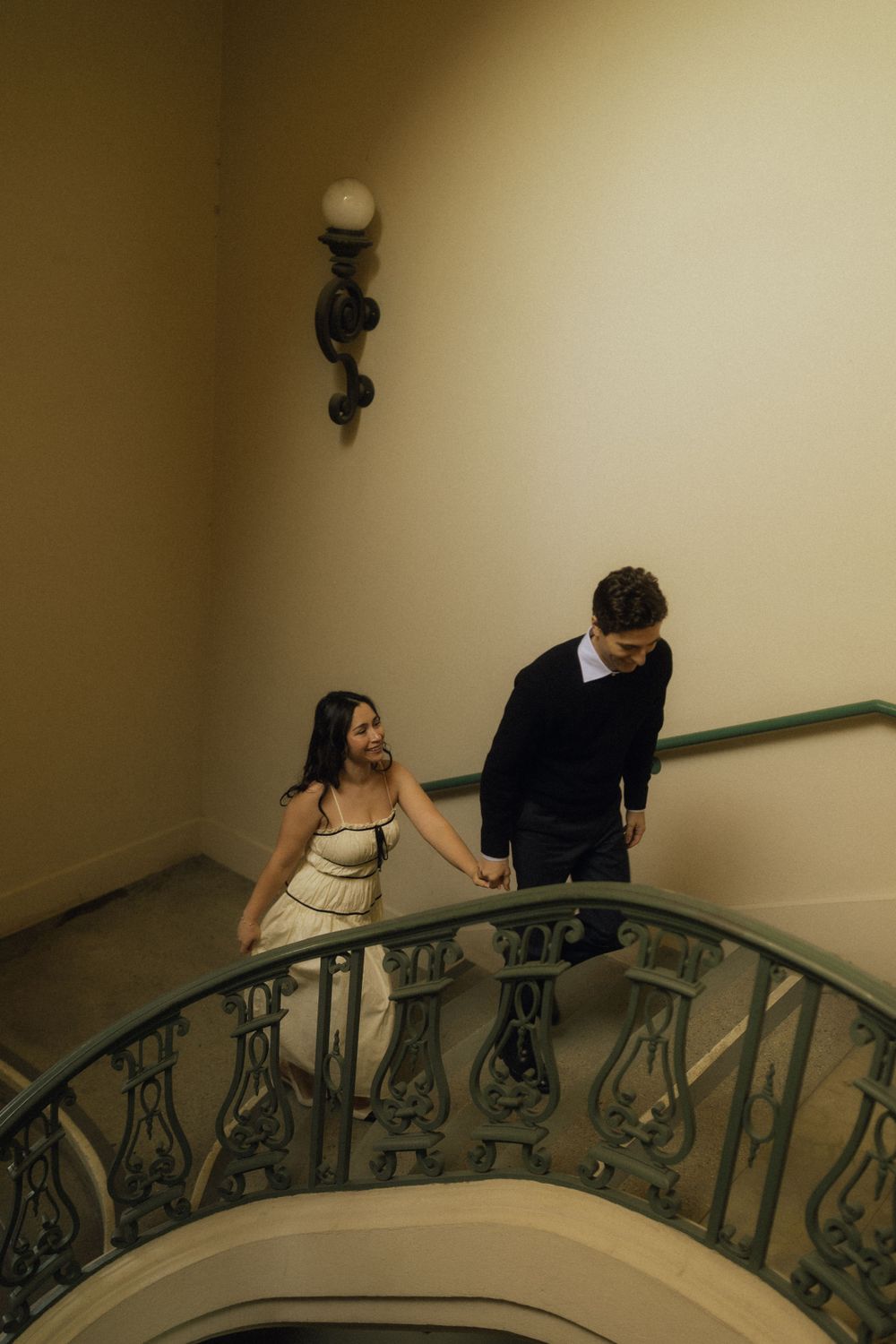 A couple descends an elegant spiral staircase with ornate iron railings.