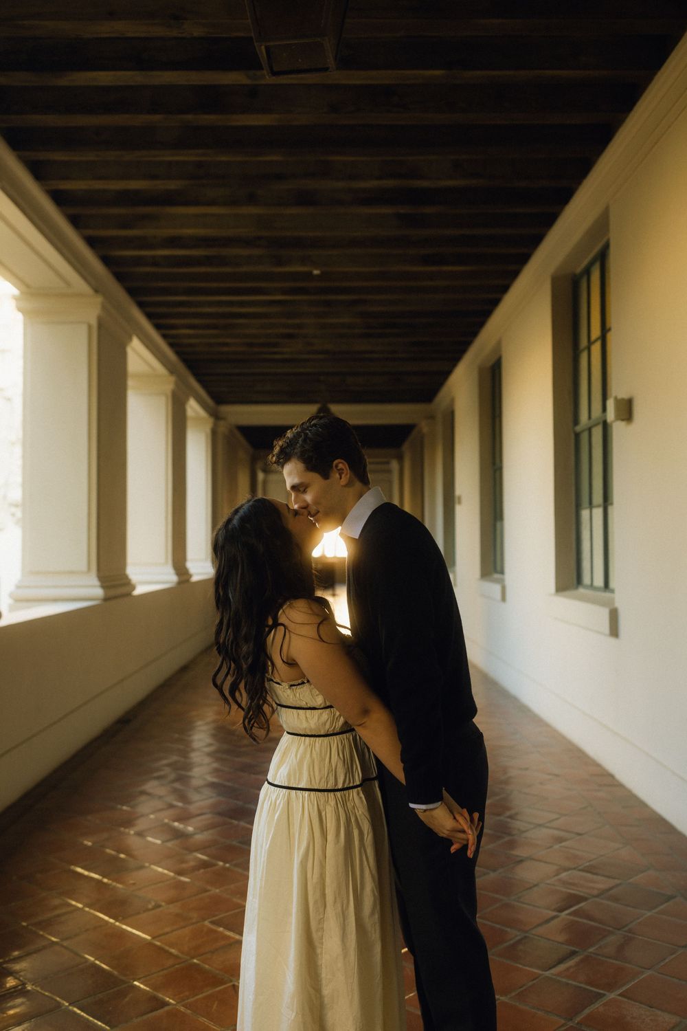 A romantic moment captured in a sunlit colonial-style hallway with terracotta flooring.
