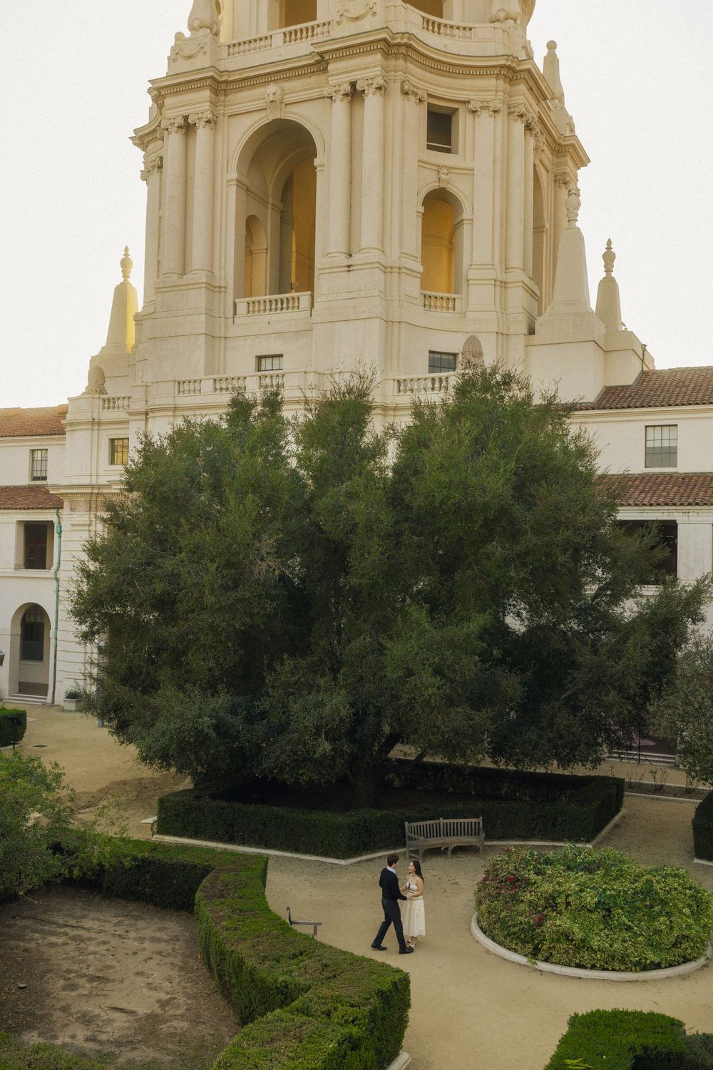 A grand Spanish colonial style building with white architecture and a tower, featuring manicured gardens and pathways.
