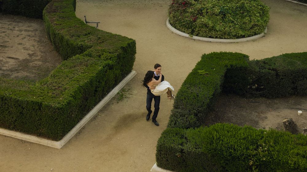 A couple embraces in a formal garden with perfectly trimmed hedges and curved pathways.