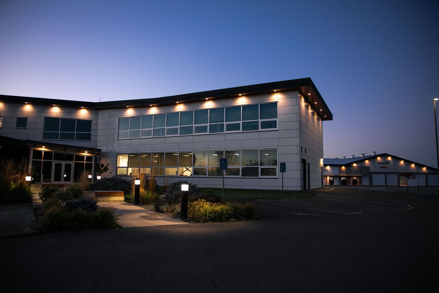 Modern office building illuminated at dusk with exterior pathway lights creating a welcoming atmosphere.