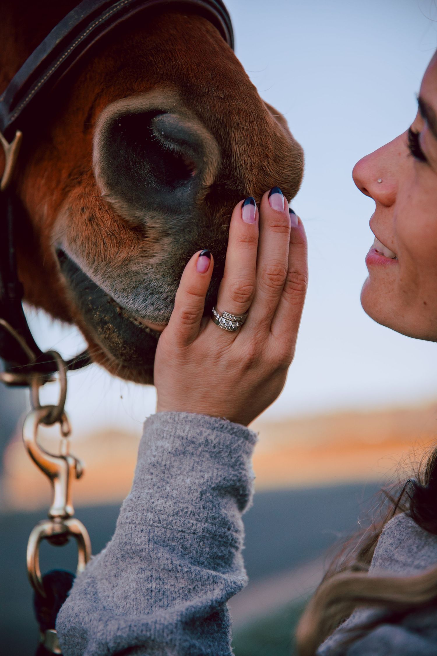 Close-up of hand tenderly touching horse's muzzle with engagement ring visible.