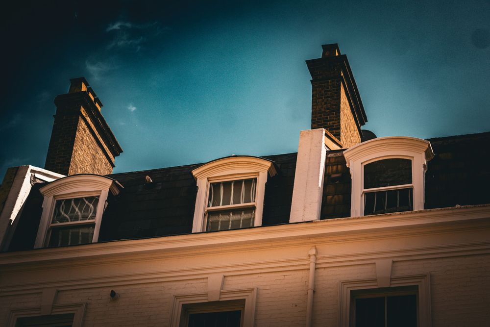 Architectural detail of dormer windows and chimneys on a classic building rooftop.