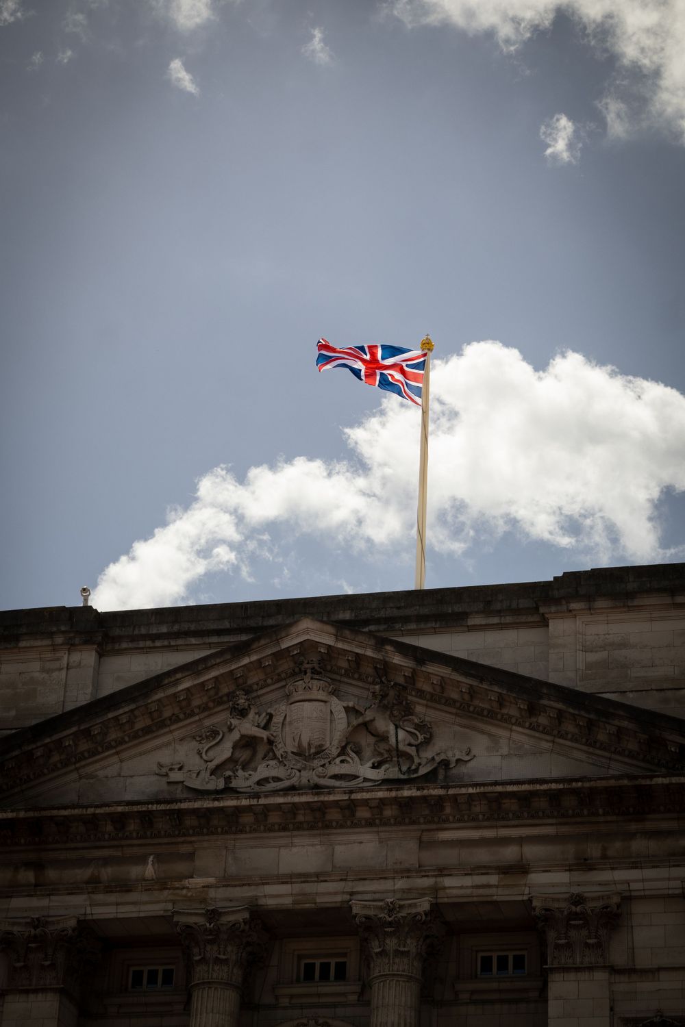 Union Jack flag flying atop ornate building facade against dramatic cloudy sky.