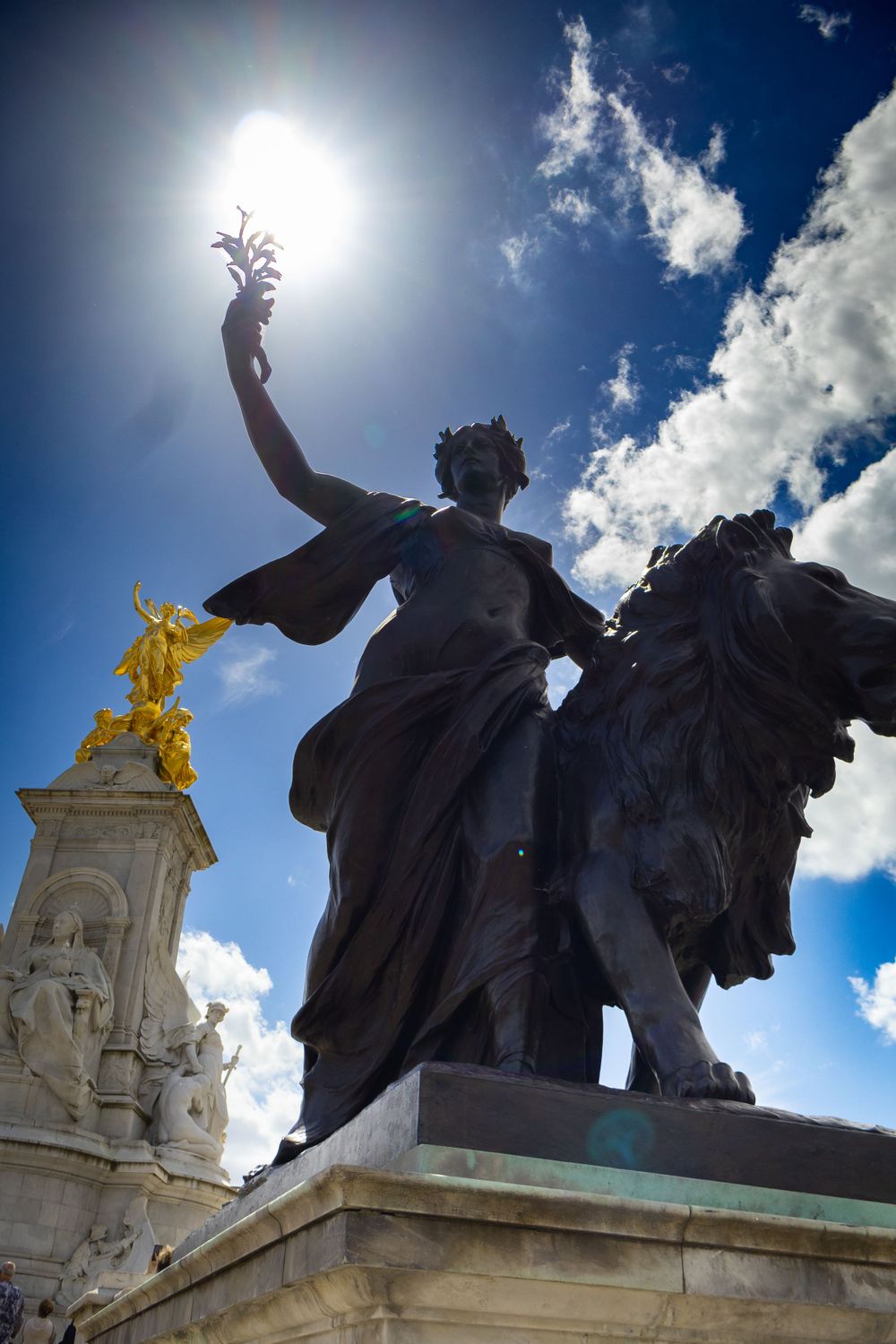 Dramatic silhouette of Victoria Memorial statues against bright blue London sky.