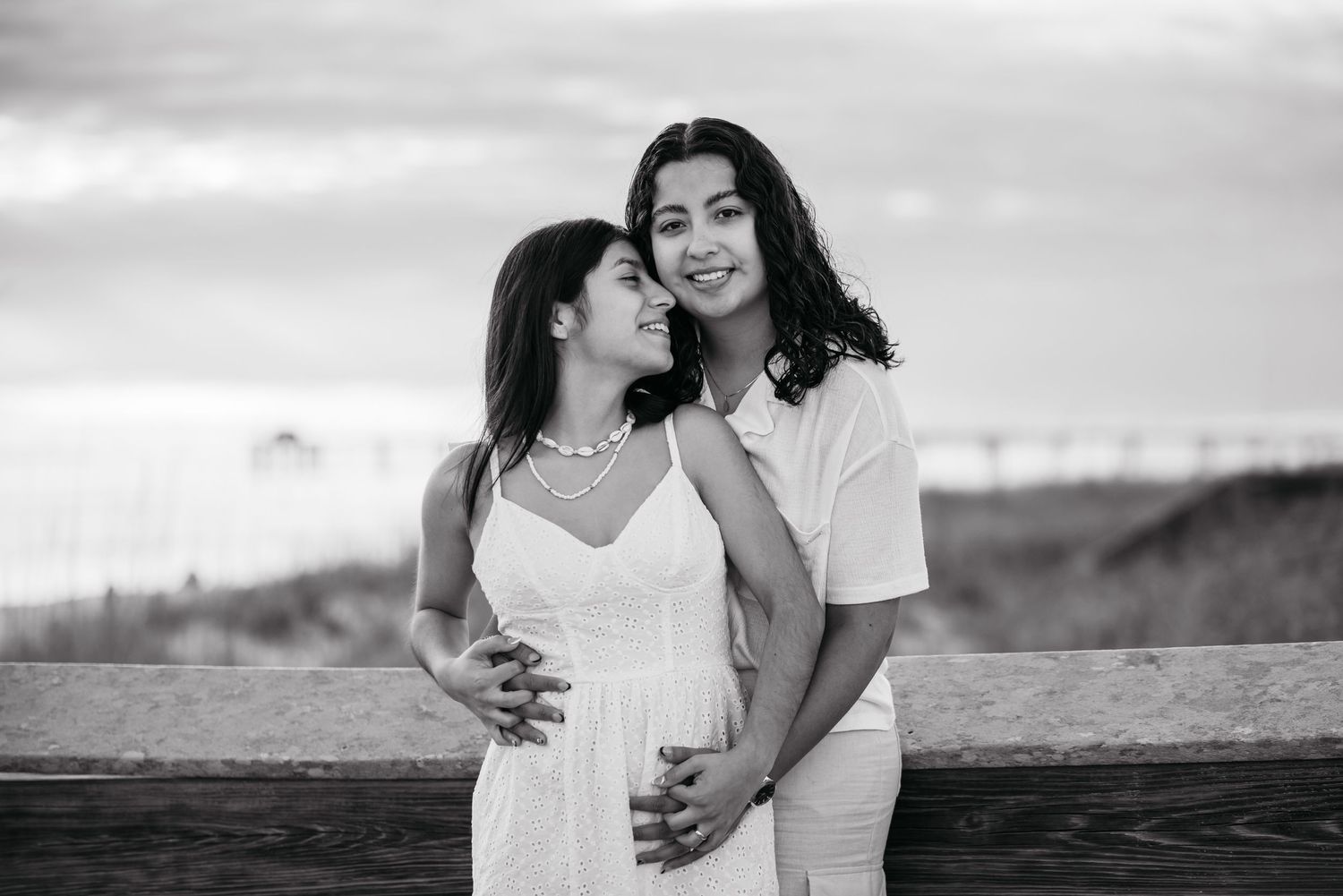 A romantic black and white portrait of a couple embracing on the beach.