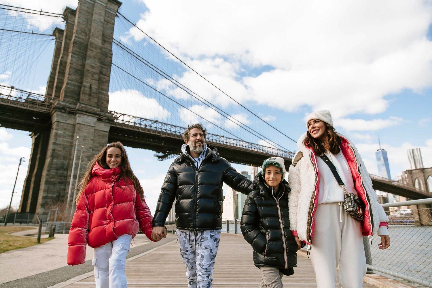 Group walking together under Brooklyn Bridge on sunny winter day.