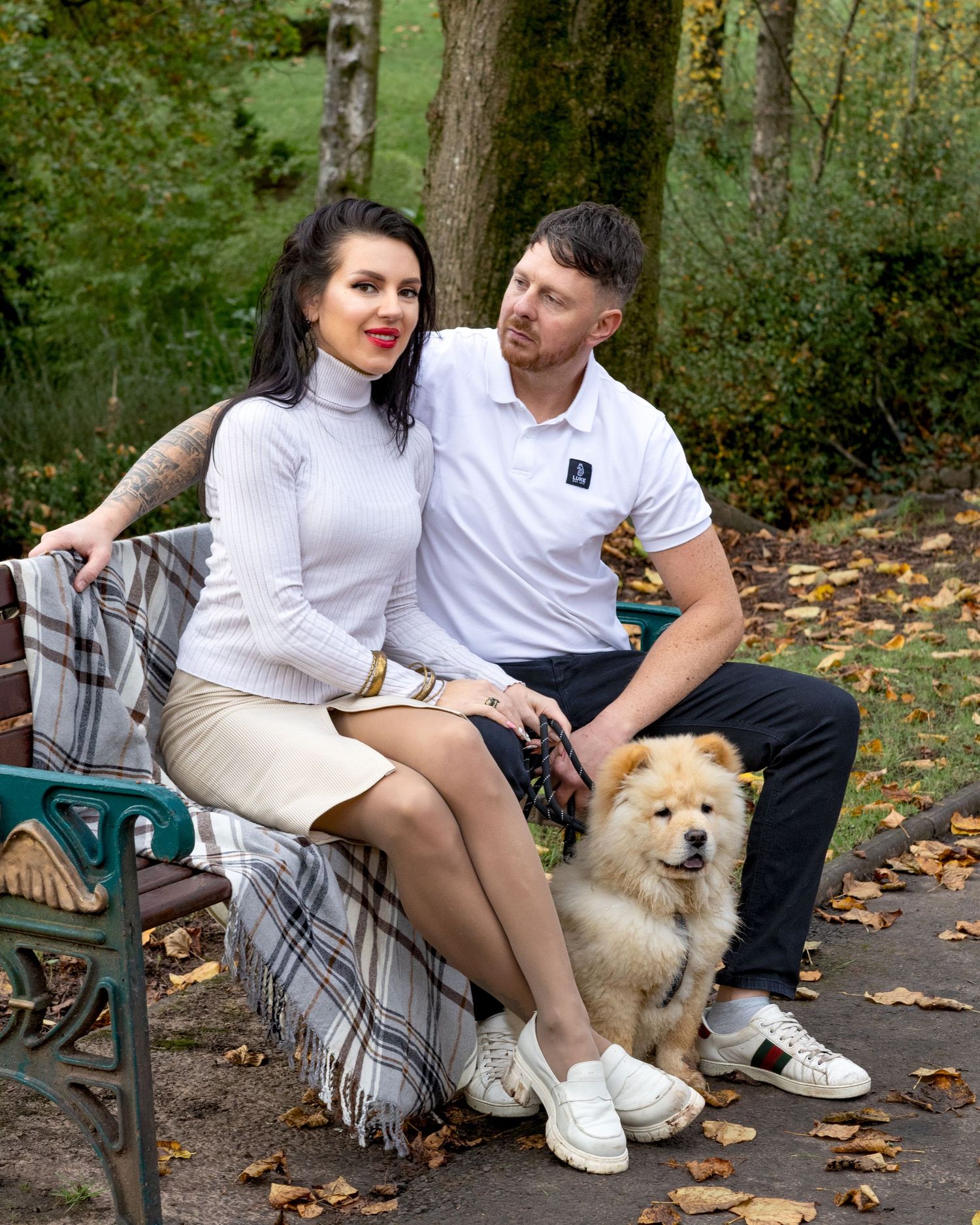 Couple sitting on park bench with fluffy Chow Chow dog during autumn.