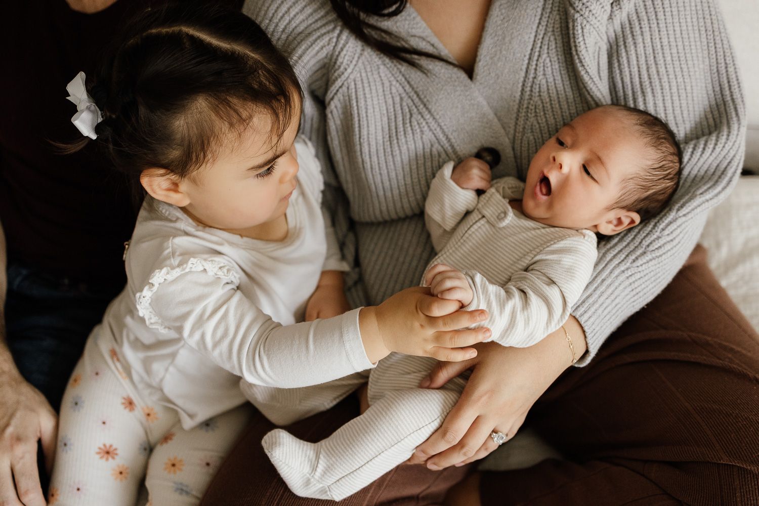 A baby's sibling holds his hand during their family's in-home lifestyle newborn photography session in San Jose