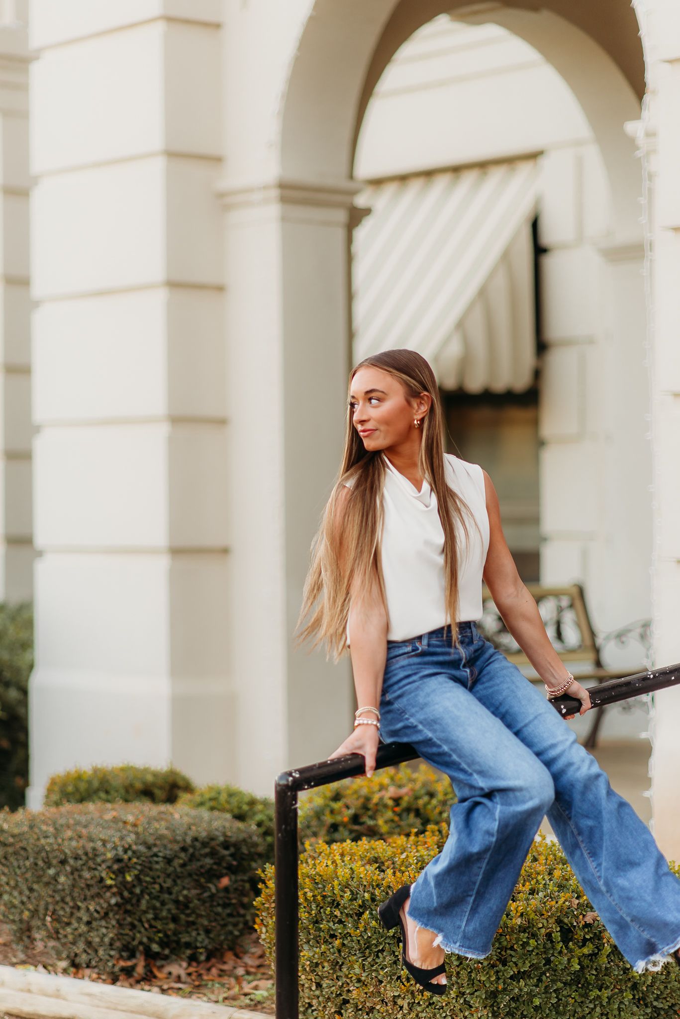 Casual fashion pose on stone railing wearing white top and flared jeans.
