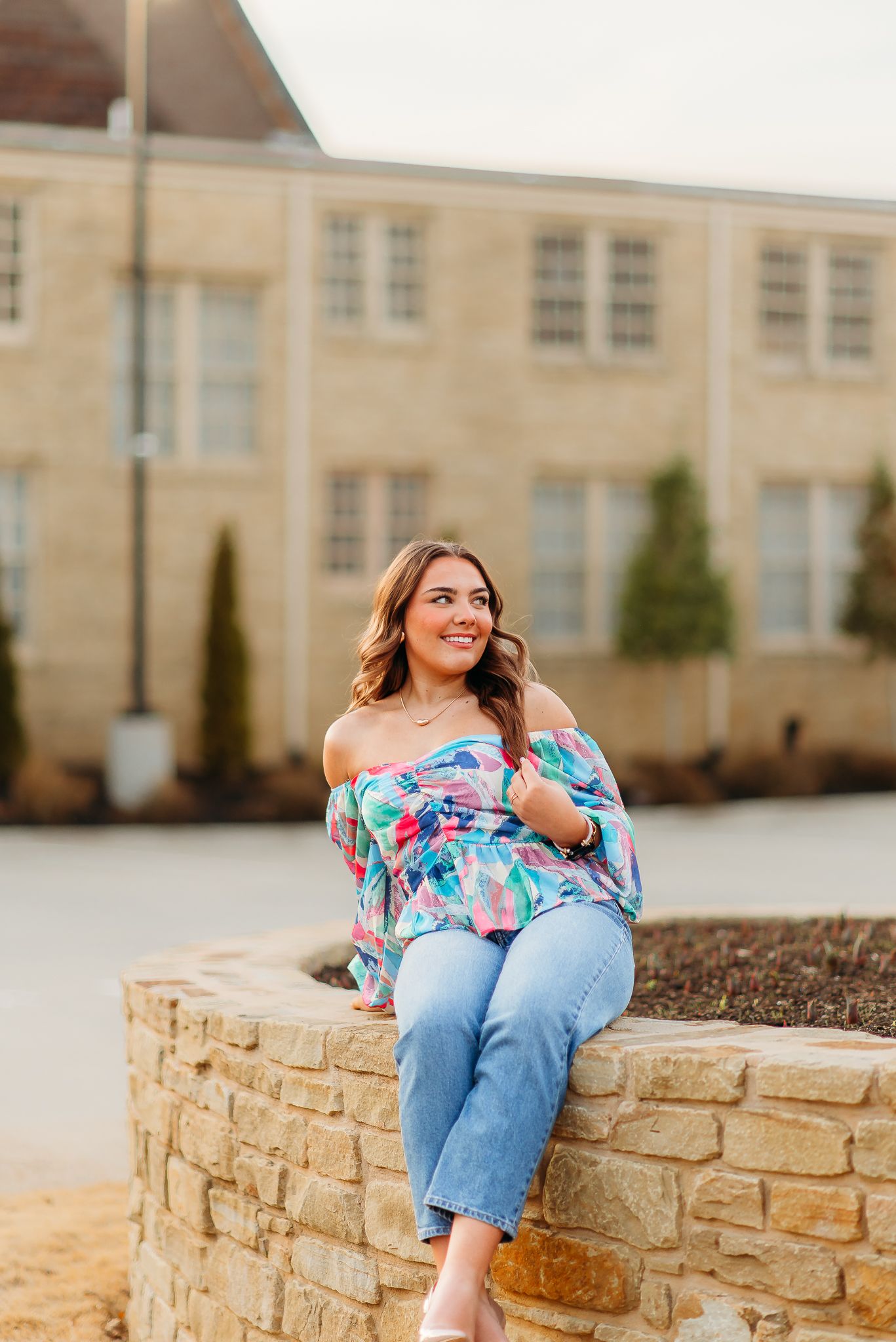 A casual outdoor portrait on a stone wall wearing a floral top and jeans.