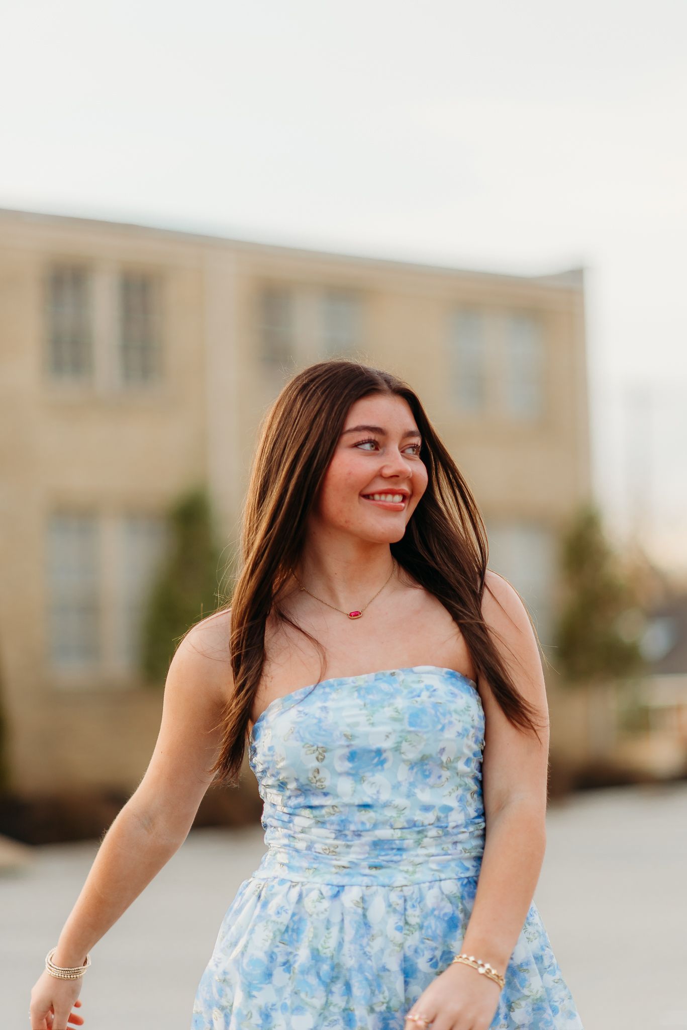 A person in a blue floral dress poses outdoors with a building in the background.