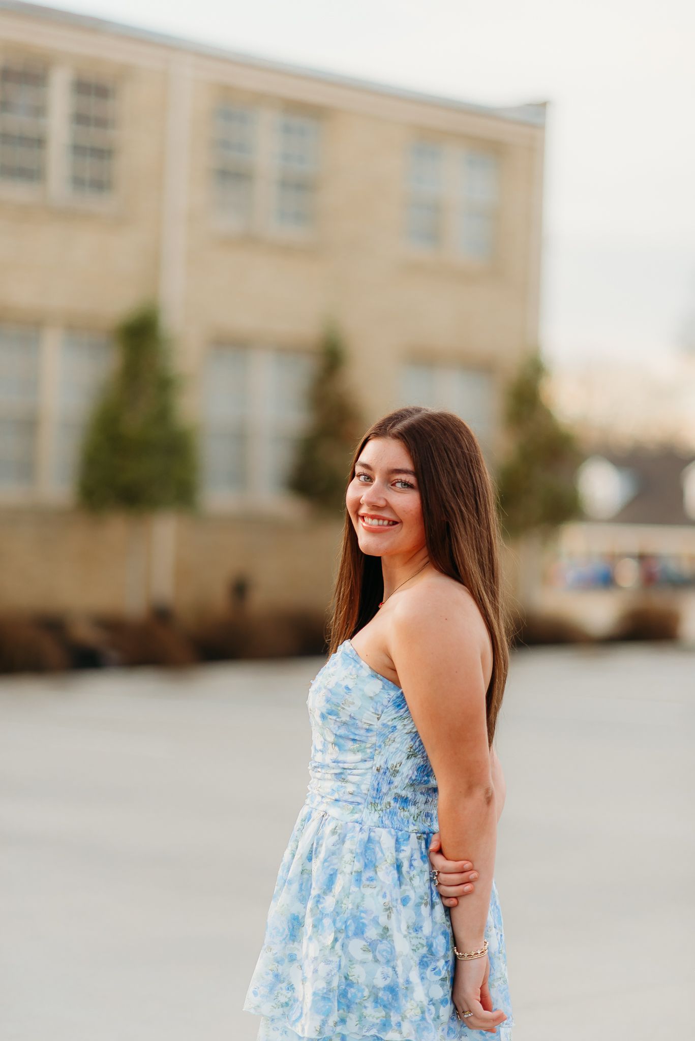 A portrait of someone in a blue floral dress standing outside a building.