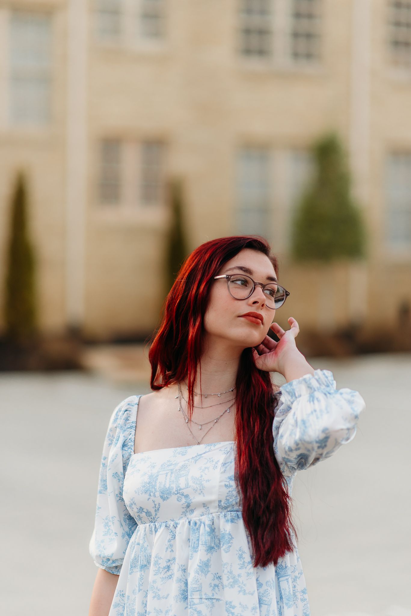 A stylish portrait featuring someone in a blue dress with long red hair and glasses.