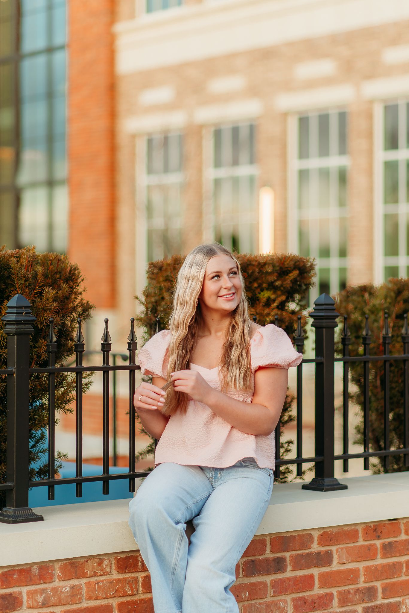 A casual portrait of someone sitting on a brick wall wearing light denim and pink.