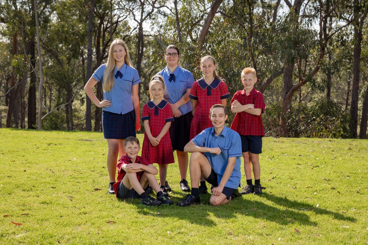 Students in school uniforms gather on a sunny grassy hillside for a group photo on campus.