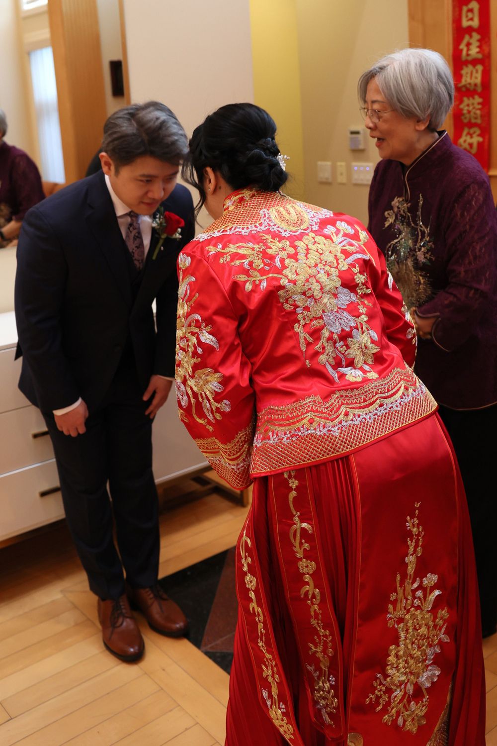 Traditional Chinese wedding ceremony with person wearing ornate red and gold embroidered dress greeting guests in hallway.